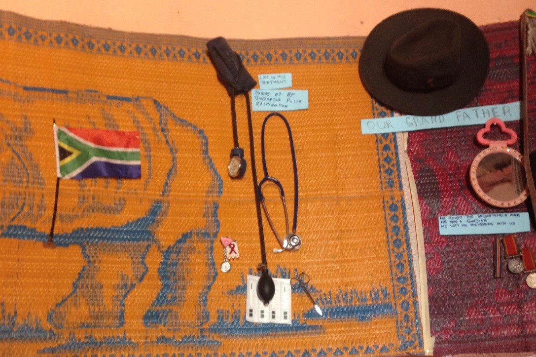 Caption: Indumba/THP consultation space of a nurse â Limpopo. Stethoscope and blood pressure machine on the wall next to her grandfatherâs hat, mirror and medals for fighting in the second world war. She had labelled these, alongside many o