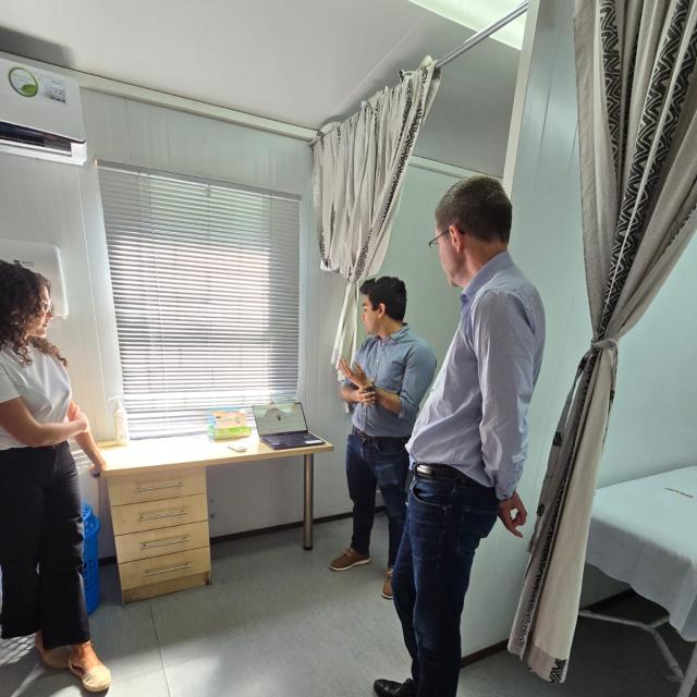 Three people standing in a clinic room with curtained cubicles