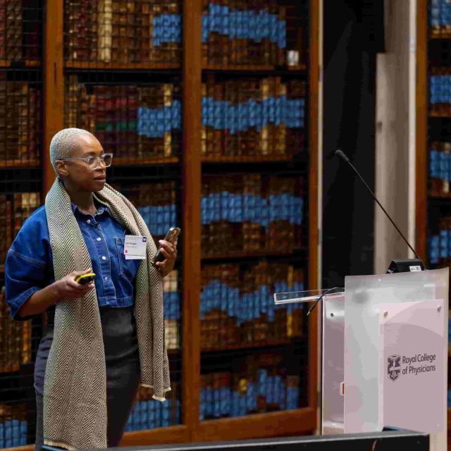 Prof. Molebogeng Rangaka speaks in a library. To her left is a lectern