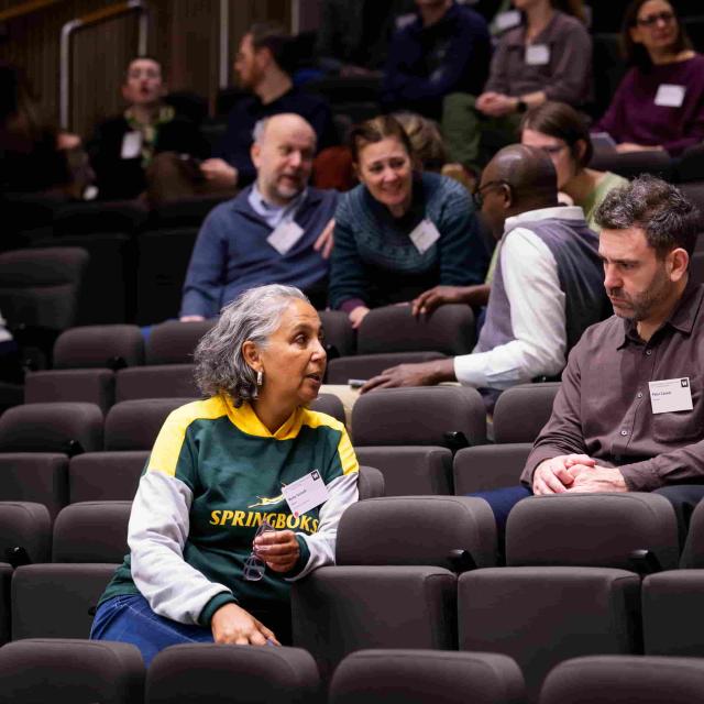 Ms Rene Goliath speaks with two other meeting participants in the raked seating of an auditorium