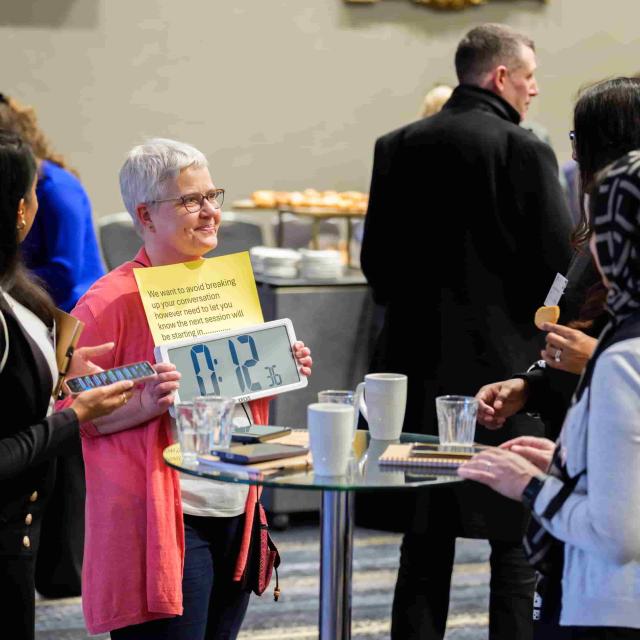 A facilitator in a pink shirt shows meeting participants an electronic countdown to the next session start